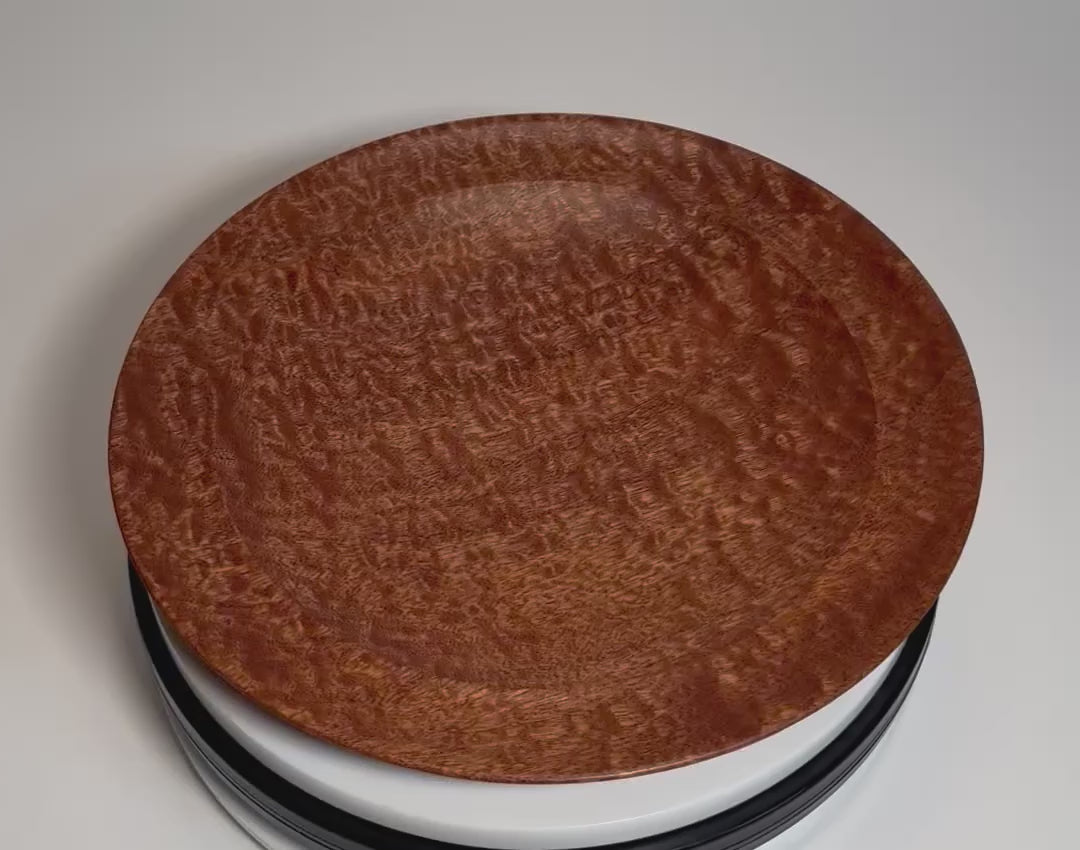 Hand-turned pommele sapele wooden bowl rotating on display stand, showcasing full-surface chatoyant dapple figure and rich mahogany tones shifting from all angles