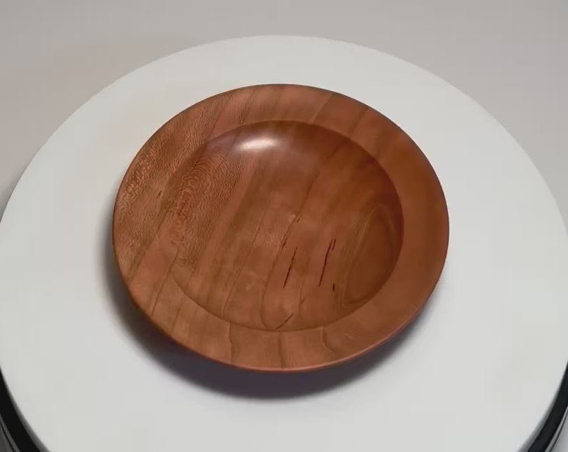 Quartersawn wild black cherry wood ring dish rotating 360 degrees on display stand, showcasing warm pink and copper tones, amber-outlined growth rings, and hand-turned form