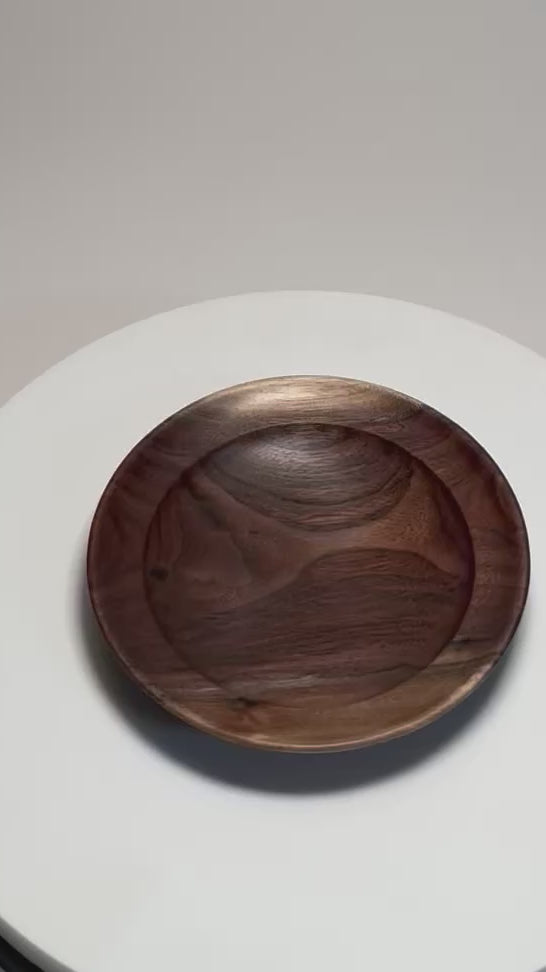 Hand-turned wild black walnut ring dish rotating on display stand, showcasing sapwood and heartwood contrast, bud scars, and flowing grain from all angles
