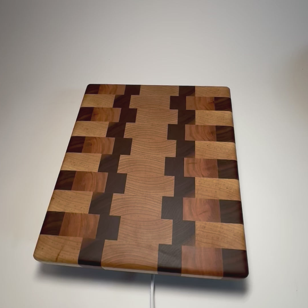 Maple, walnut and cherry end grain cutting board on a rotating display, showing its geometric wood pattern and thick edges.

